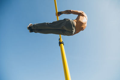 Rear view of man hanging on bar against sky