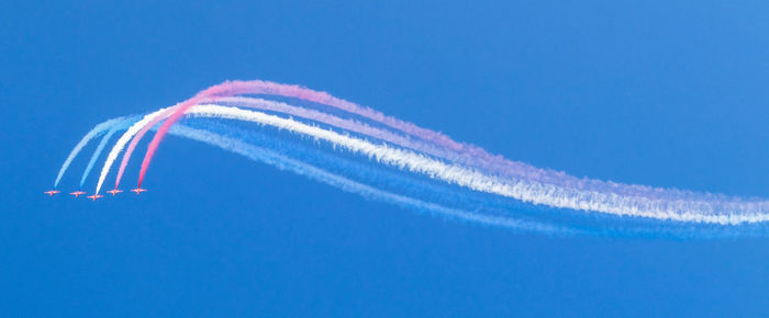 Low angle view of jet aerobatics against blue sky