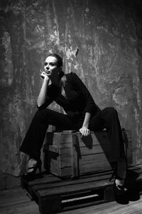 Woman with hand on chin looking away while sitting on wooden box against wall