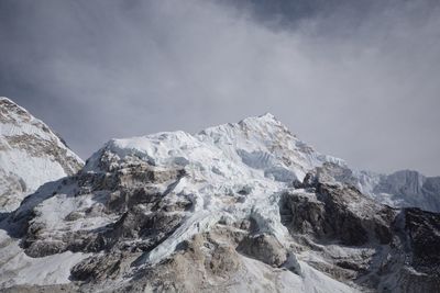 Low angle view of snowcapped mountains against cloudy sky on sunny day