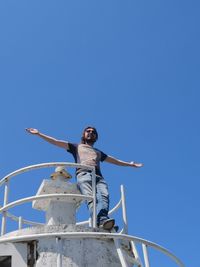 Low angle view of man standing with arms outstretched against sky