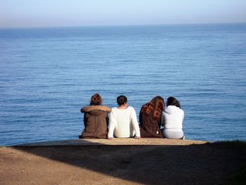 Rear view of female friends sitting by sea