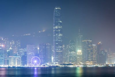 Illuminated modern buildings in city against sky at night