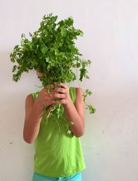 Boy holding herbs while standing against wall