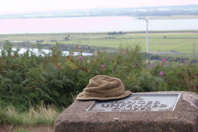 Close-up of hat on stone with warning sign by field