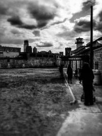 People walking on city street against cloudy sky