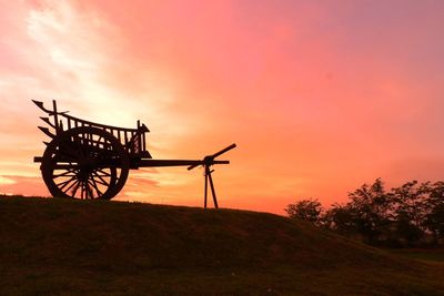 Silhouette cranes on field against sky during sunset