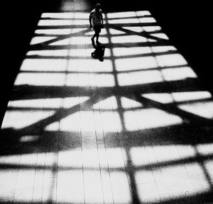 High angle view of man walking on footpath with shadow pattern during sunny day