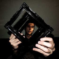 Portrait of young man looking through picture frames