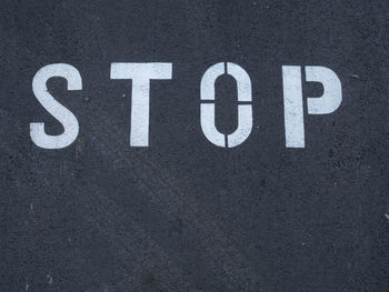 White stop sign painted on asphalt. you can see tire tracks over it. indicates a mandatory stop.