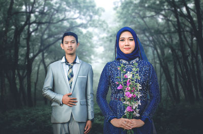 Portrait of young couple standing against trees