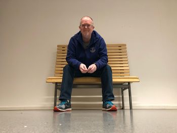 Portrait of man sitting on bench against wall