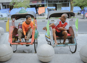 Men sitting on chair by street in city