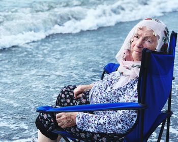 Portrait of woman sitting on chair at beach