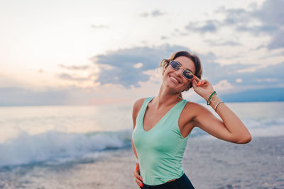 Young woman standing at beach against sky during sunset