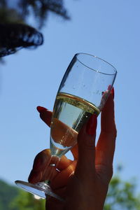 Cropped image of hand holding beer glass against clear sky