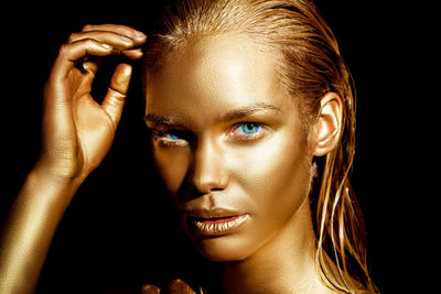 Close-up portrait of woman with golden glitter make-up against black background