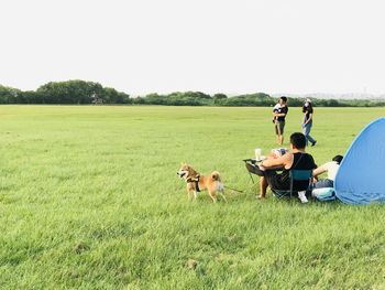 People sitting on field by land against sky