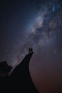 Couple standing on the edge of a cliff during the night sky
