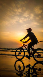 Silhouette man riding bicycle on beach against sky during sunset