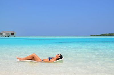 Woman lying on beach against clear sky
