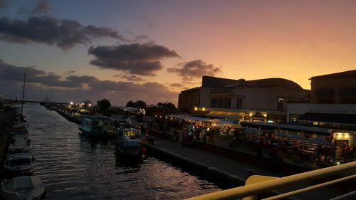 Boats moored at harbor by buildings against sky during sunset