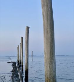 Wooden posts in sea against clear sky