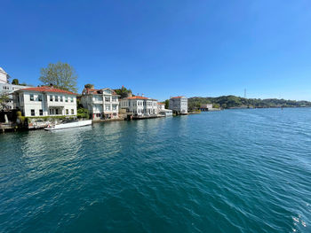 Buildings by sea against clear blue sky