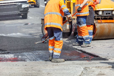 A group of road workers are repairing a section of the carriageway by rolling up fresh asphalt.