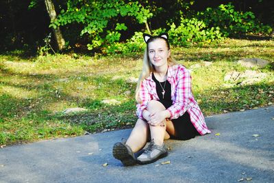 Portrait of smiling young woman sitting on road against plants