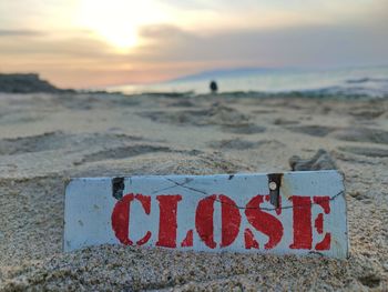 Close-up of a plate on which is mentioned close on beach against sky during sunset