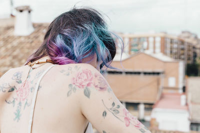 Rear view of woman with tattoo against buildings and sky