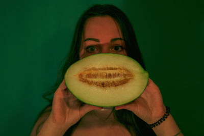 Portrait of woman holding melon against wall