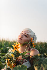 Portrait of young woman with sunflower on field against sky