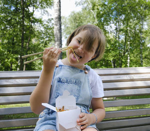 Teenage girl on a walk on a summer day in the park has lunch with noodles wok