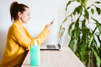 Side view of woman using smart phone by laptop at home