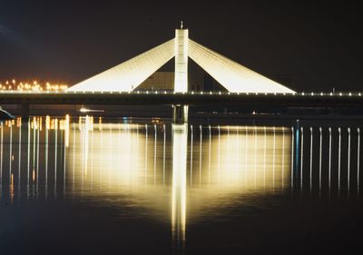 Illuminated bridge over river against sky at night