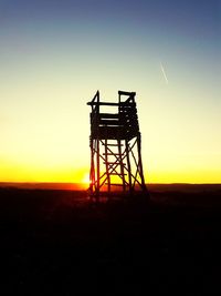 Silhouette crane on field against clear sky