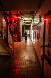 Rear view of woman walking in illuminated corridor