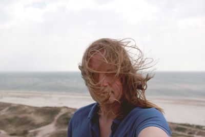 Portrait of man with long hair at beach against sky