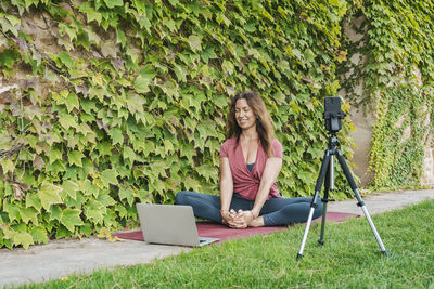 Woman using mobile phone while sitting on plant