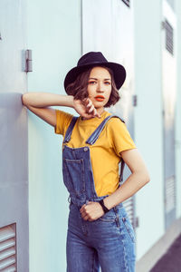 Young woman looking away while standing against wall