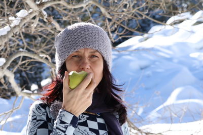 Portrait of mature woman eating fruit against bare tree