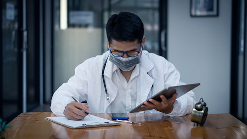 Doctor wearing mask writing on note pad at clinic