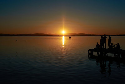 Silhouette people in sea against sky during sunset