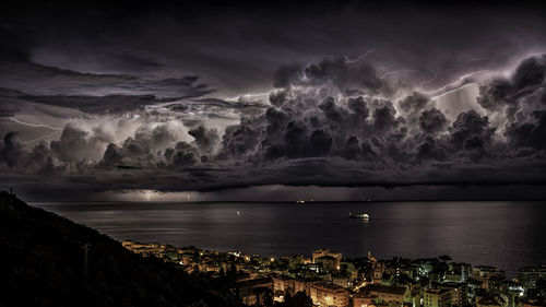 Modern buildings by sea against cloudy sky at night