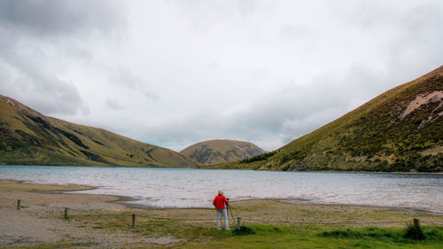 Rear view of woman standing by lake against sky