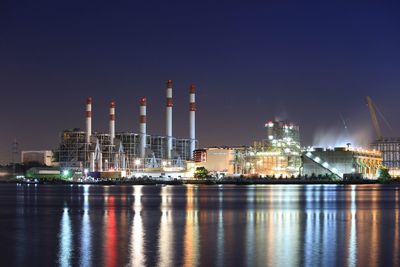 Illuminated buildings by river in city against sky at night