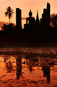 Reflection of silhouette built structures in water at sunset