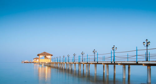 Stilt house on lake against clear blue sky